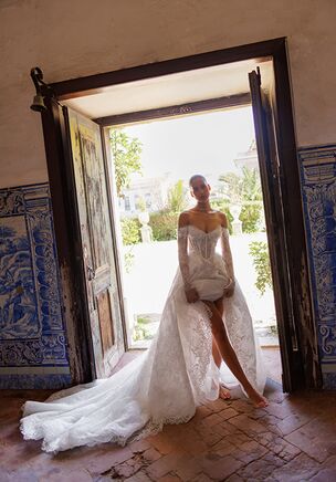 A stunning A-line silhouette gown crafted from delicate Chantilly lace with intricate appliqué adorning the corset. This dress showcases a luxurious lace ensemble, exuding timeless elegance and romance. The top layer of the skirt is gracefully fixed in place, adding dimension and movement to the design. The long sleeves fasten with discreet zippers for a refined touch. The corset features a lace-up back, ensuring a perfect fit, while the gown is completed with an elegant, flowing train for a truly regal look.