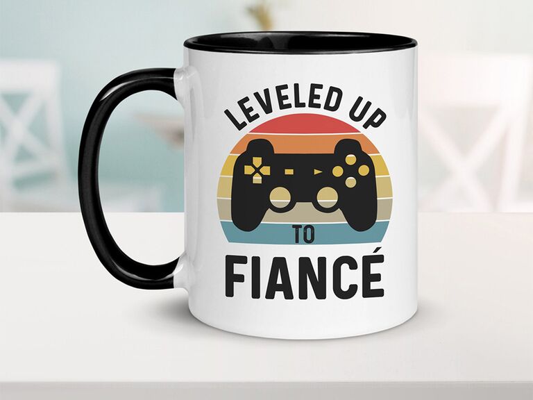 'Leveled up to fiancé' in bold black sans serif type with game controller graphic on colorful half circle background