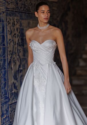 The dress is made of Mikado fabric, featuring an A-line silhouette with a mermaid-style illusion. The sweetheart neckline adds a romantic touch. The dress is adorned with draping, pearls, and floral appliqués. The skirt is non-detachable and fixed at the front. The corset fastens with lacing. The back of the dress is decorated with floral appliqués and pearls only in the upper part. Accessorized with a dramatic voluminous overskirt, Birgit takes on extra volume for a grand down-the-aisle entrance.