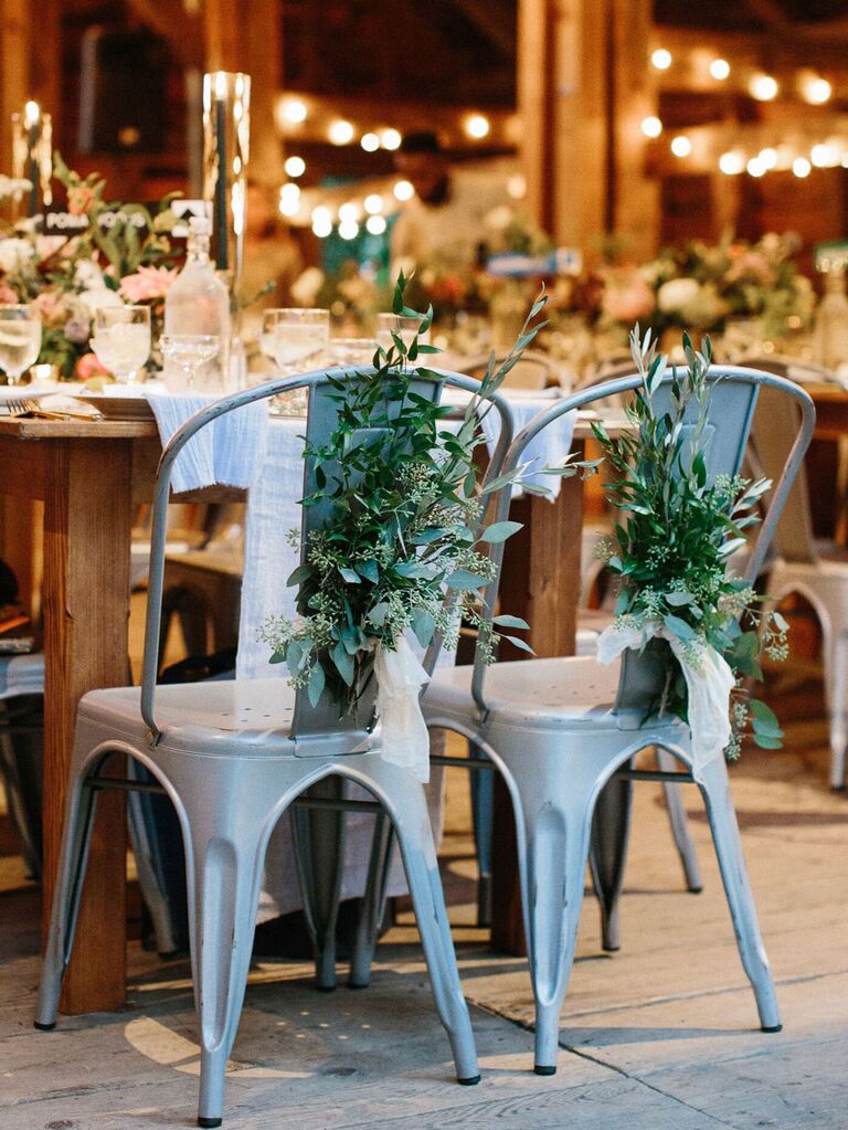 Industrial metal sweetheart chairs with sprigs of greenery at rustic barn wedding