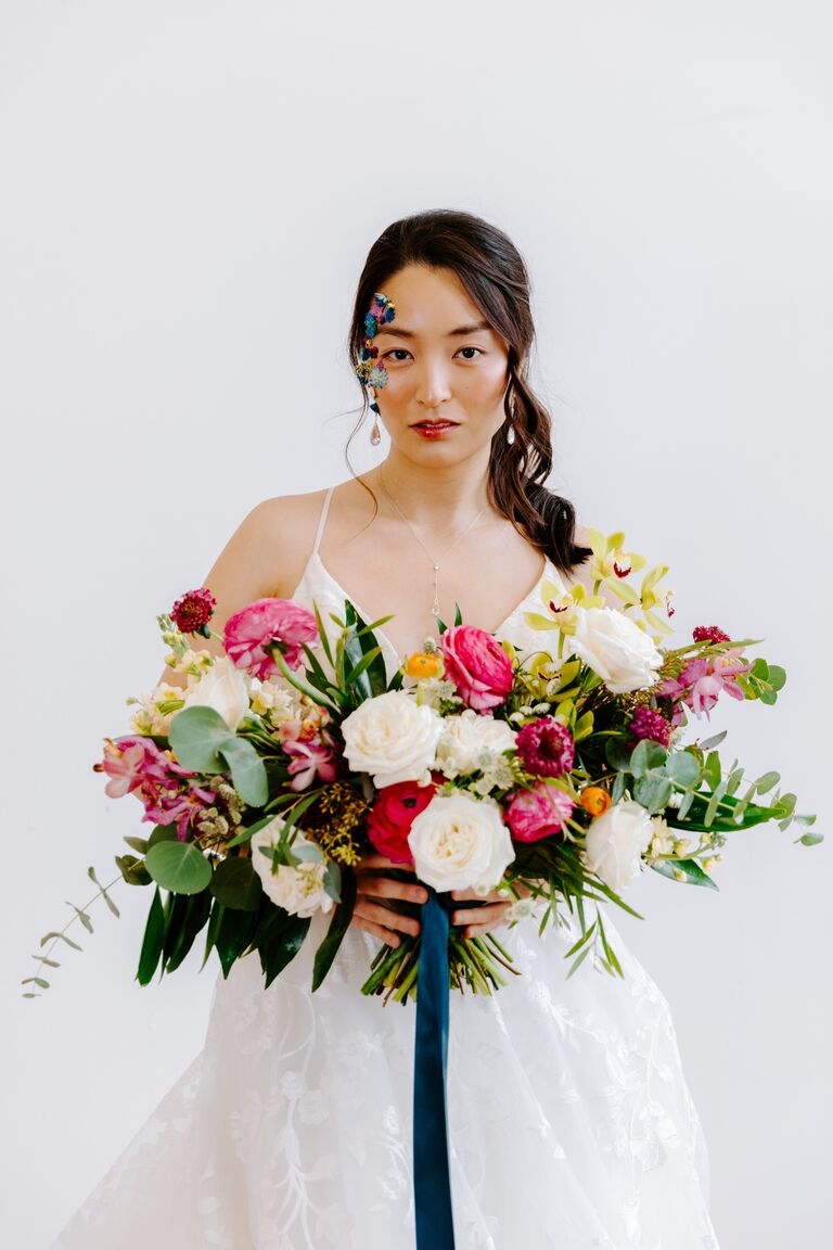 bride holding colorful wedding bouquet full of 2021 wedding colors hot pink yellow green white flowers and dark blue ribbons