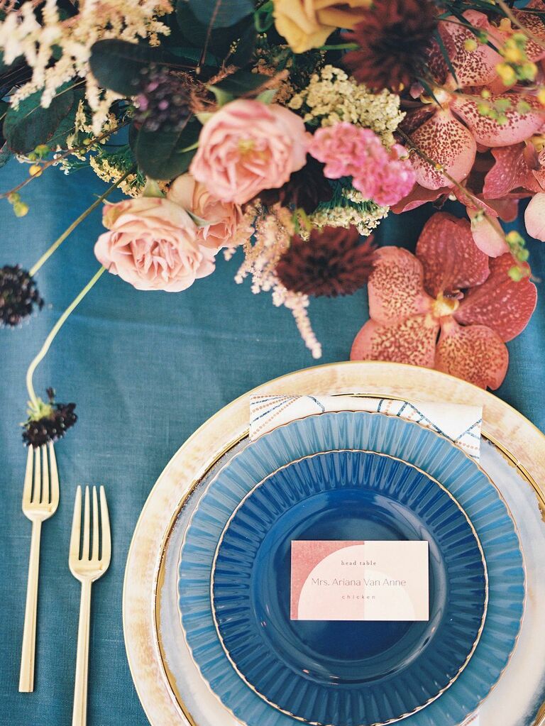 fall place setting with navy blue tablecloth, gold charger plate and burgundy centerpiece