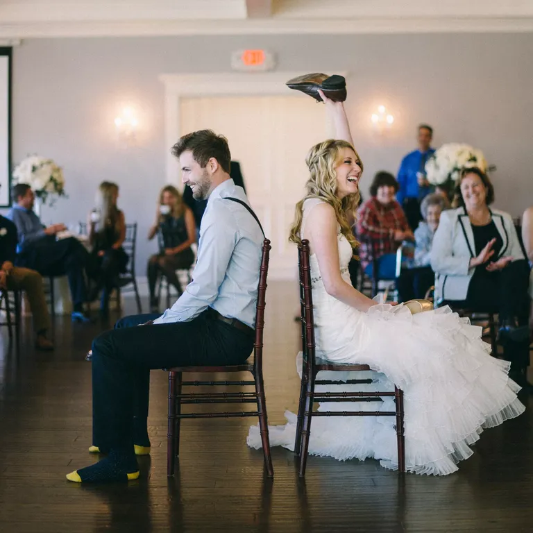 Bride and groom sitting in chairs back to back playing shoe game at reception