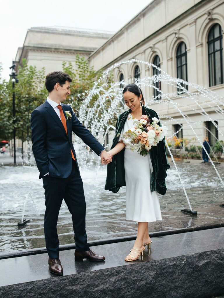 Couple hold hands in front of an urban fountain. 