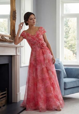 Romantic and eye-catching, this Heather Print Organza A-line gown is a beautiful choice for the Mother of the Bride. The open portrait neckline creates an elegant frame, while the gathered bodice adds soft shape and movement. A delicate flower accent at the natural waist draws the eye, and a cascading ruffle down the front of the skirt adds graceful drama and flow. Feminine, stylish, and full of charm, this gown is designed to make a memorable statement.