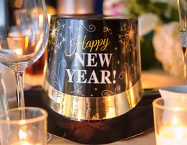 close up of new year's eve hat next to wine glasses