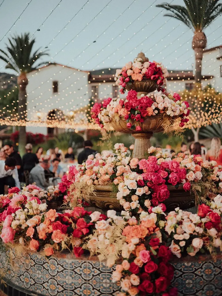 Tiered Fountain With Spilling Flower Arrangements in Pink and Blush Under String Lights
