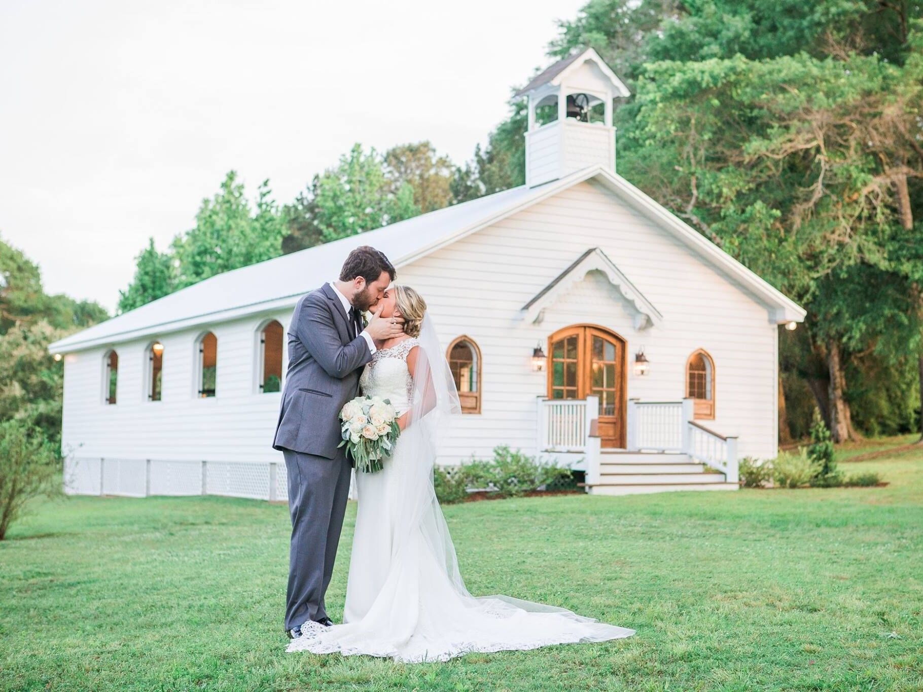 Couple kissing for a wedding portrait outside the charming white venue