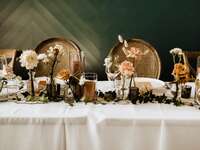 fall wedding color tablescape with white tablecloth, brown candles and mauve, cream and caramel colored roses in mismatched glass vases
