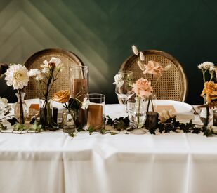 fall wedding color tablescape with white tablecloth, brown candles and mauve, cream and caramel colored roses in mismatched glass vases