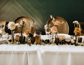 fall wedding color tablescape with white tablecloth, brown candles and mauve, cream and caramel colored roses in mismatched glass vases