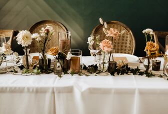 fall wedding color tablescape with white tablecloth, brown candles and mauve, cream and caramel colored roses in mismatched glass vases