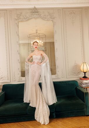 Perfectly fitted and corset based dress finely decorated with handcrafted appliquès, lace and pearl-beads along the neckline and upper sleeves. The mermaid-tail descends to the bottom, creating a delicate train. Detachable elements feature cold-shoulder beaded ruched sleeves and transparent gloves with simple floral appliquès as well as the veil, adding a polished look to the whole outfit.
