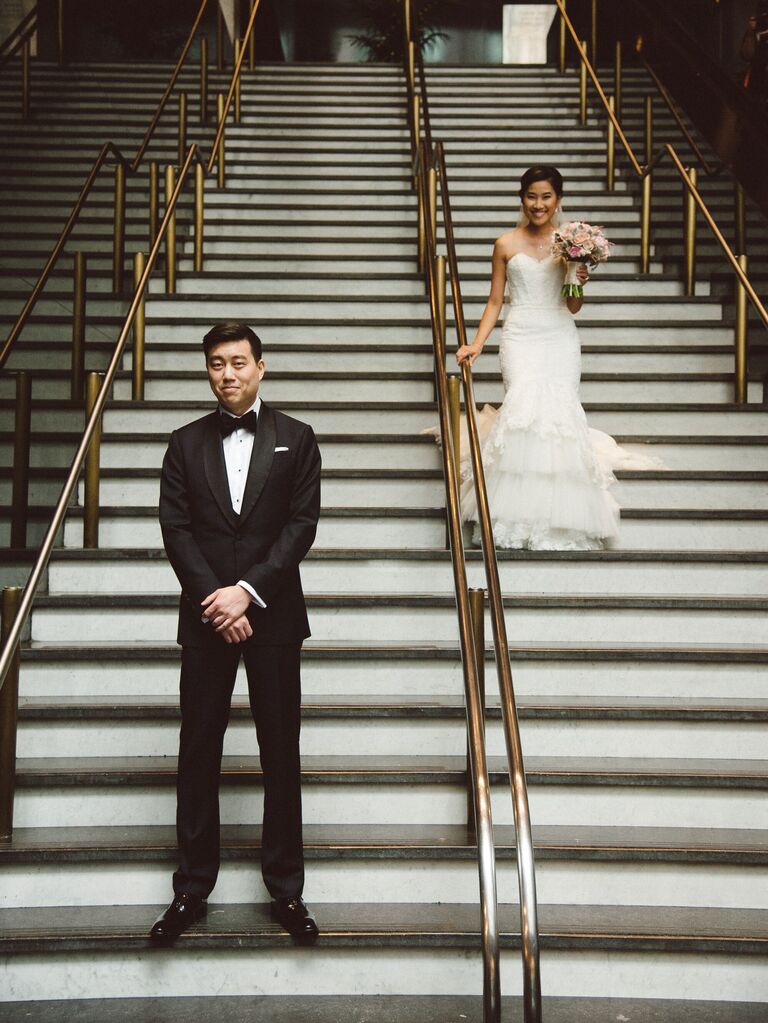 bride walks down the stairs at san francisco city hall to surprise groom with his back turned