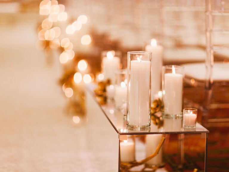 wedding ceremony aisle decor with white pillar candles in glass vases on top of a mirrored box 