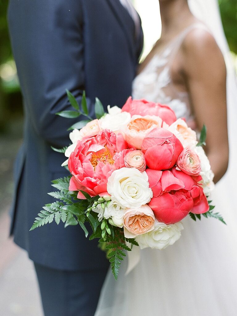 A couple stand together holding a white rose and vibrant pink peony bouquet.