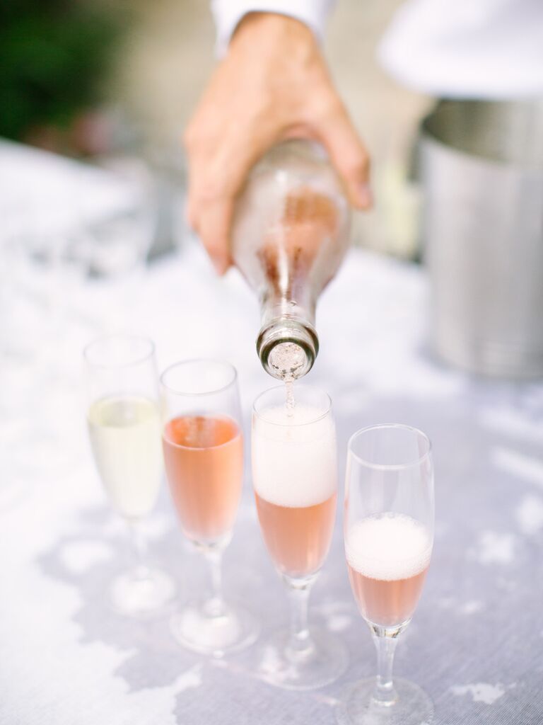 server pouring sparkling rose champagne into glass flutes