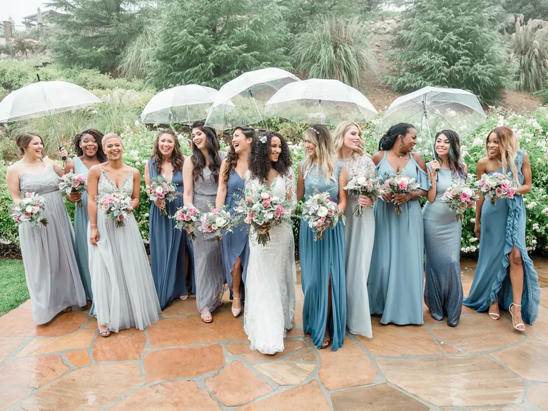 A bride smiles with her wedding party beneath see-through umbrellas.