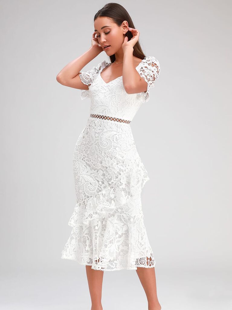 Model wears a white mid-length dress with lace detailing. 