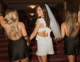 A bride walks hand-in-hand with two friends.
