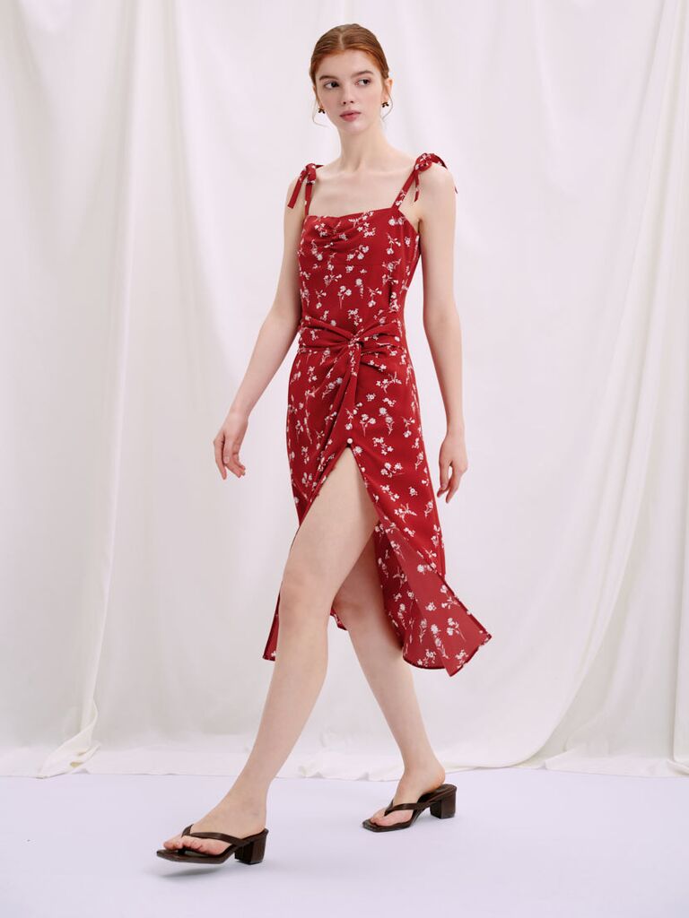 Model wears a mid-length red dress with a floral print. 