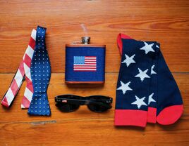 wedding accessories flat lay with red and white striped bow tie, american flag flask and navy blue star socks