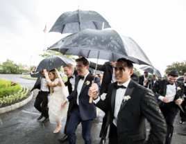 Bride, groom, and wedding party holding umbrellas and running for cover on rainy wedding day 