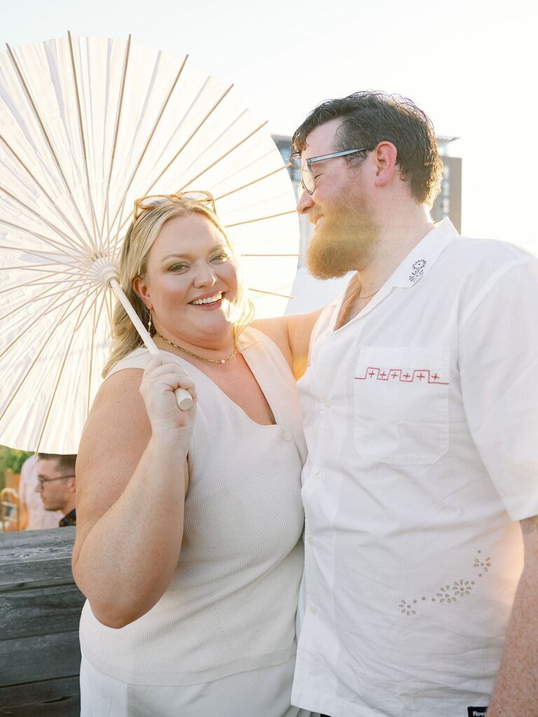 Couple wearing white casual attire posing with parasol summer engagement photo idea