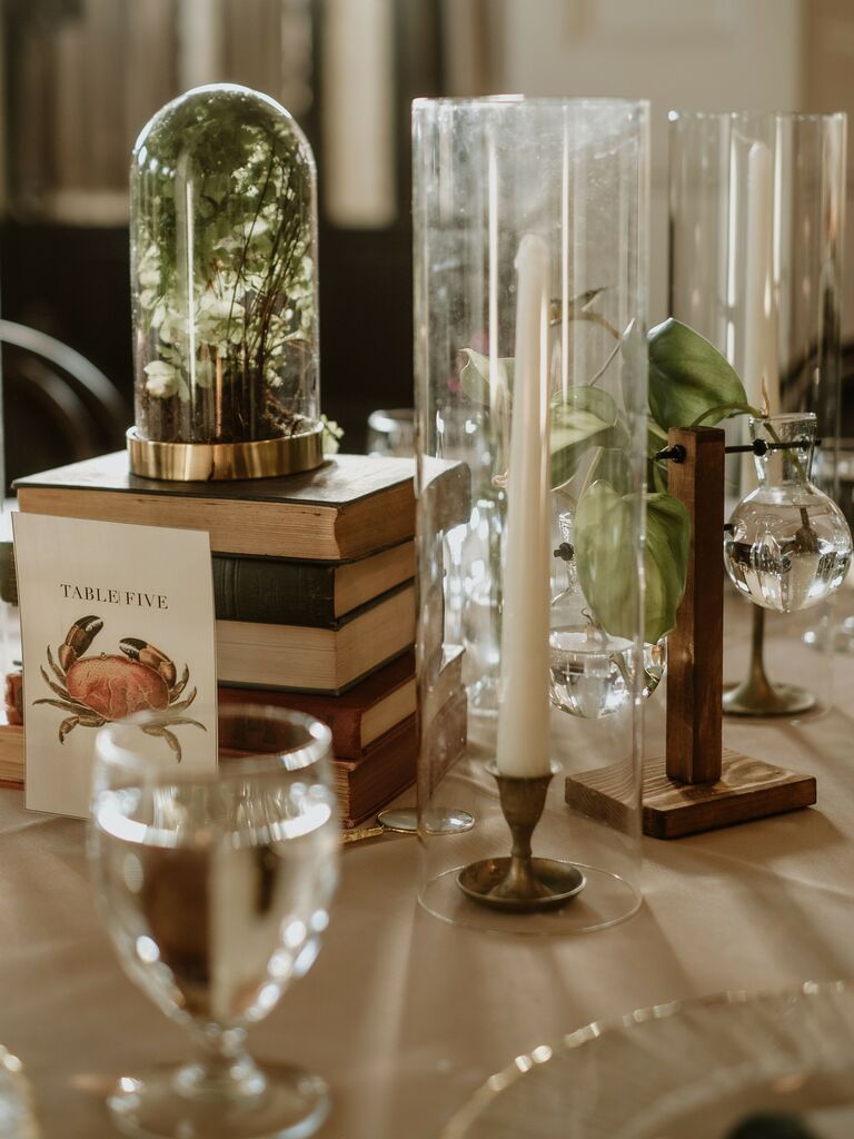 unique wedding centerpiece idea with vintage books, white taper candles and mini bell jars with greenery