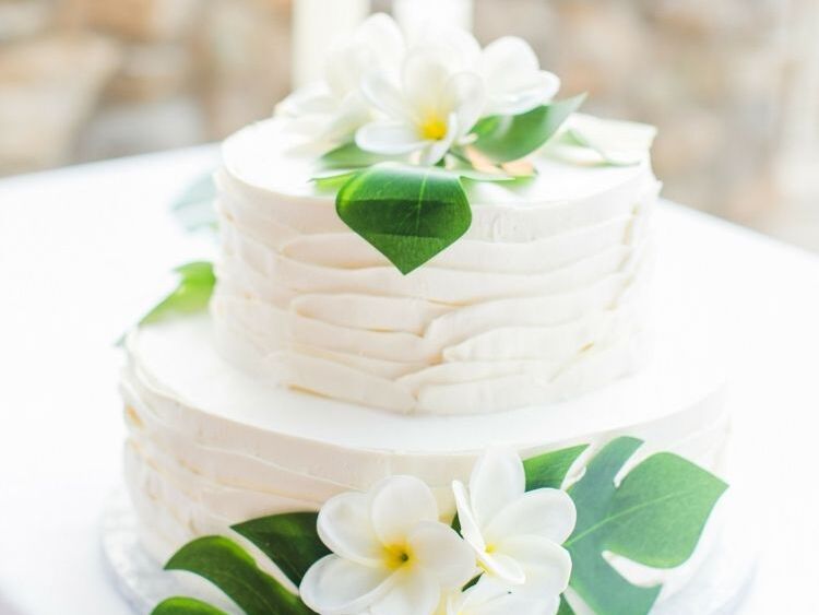 Two-tier wedding cake with monstera leaves and plumeria flowers