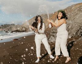 Couple pops champagne on the beach. 