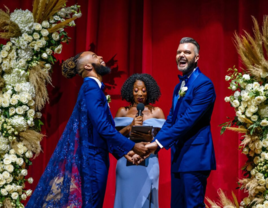 Grooms holding hands and laughing at altar