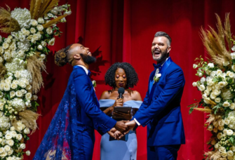 Grooms holding hands and laughing at altar