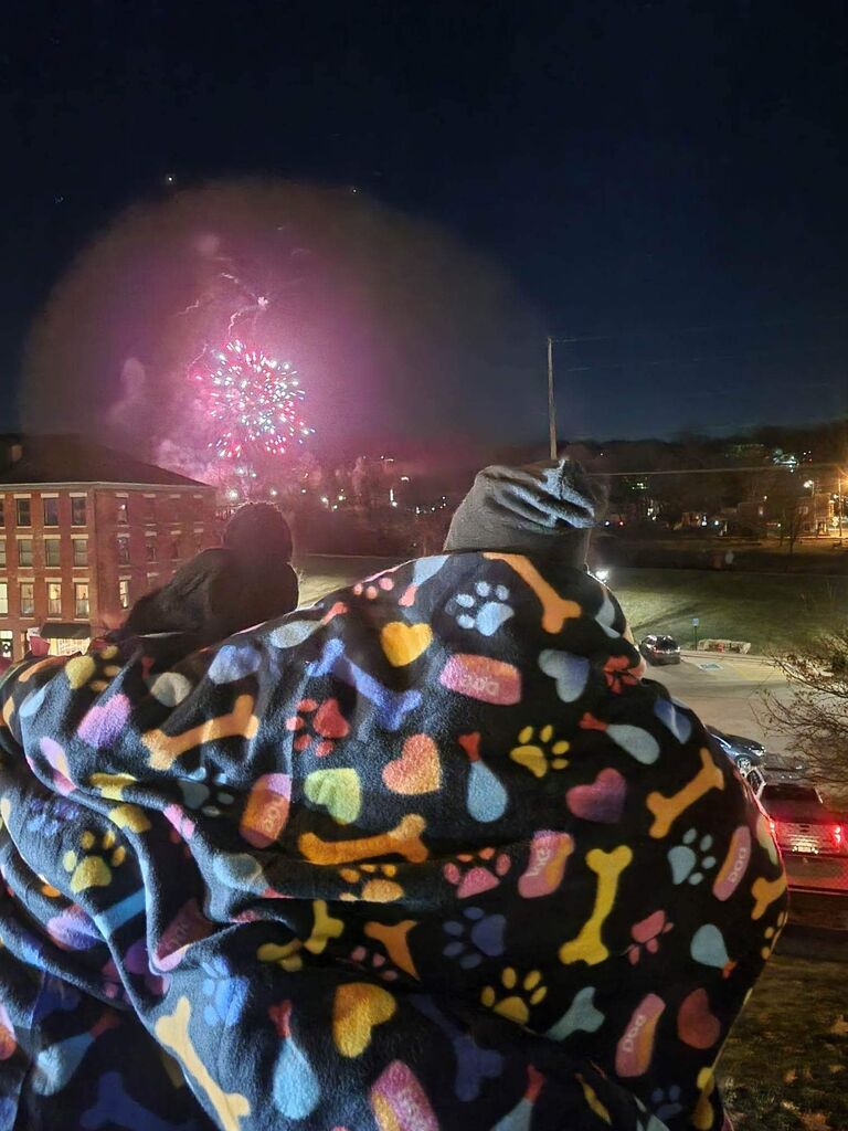 This picture was taken by my bridesmaid, Mikaela. She, Adam and I were all exploring a Christmas festival in Galena, Illinois, and the night was topped off by a fireworks display. It was absolutely frigid, and we'd had an early dinner—so our group decided to find a good spot to see the show, and then waited around in the cold, playing games and being silly. I was the only one who had dressed appropriately for the weather, so I had given out some emergency blankets from my car; this photo was shot right after the show began, and Adam slung his arm around my shoulders, to help keep me warm, too.
That was the first night I said "I love you."