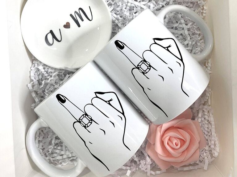 Hand holding up ring finger with engagement ring on it in black on white mug