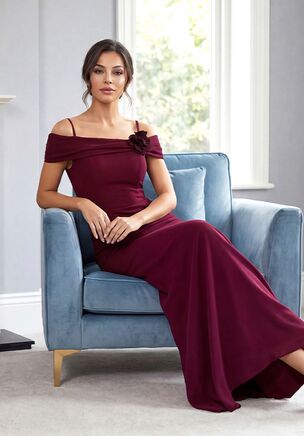 This Stretch Soft Crepe fit-and-flare gown is a stunning and modern choice for the Mother of the Bride. The portrait collar and off-the-shoulder neckline are enhanced with soft gathers and a delicate flower accent, creating a romantic and flattering silhouette. Added straps provide both support and versatile style, while the natural waistline flows seamlessly into the fit-and-flare skirt for graceful movement. Elegant, contemporary, and full of charm, this gown makes a statement while keeping comfort and sophistication at the forefront.