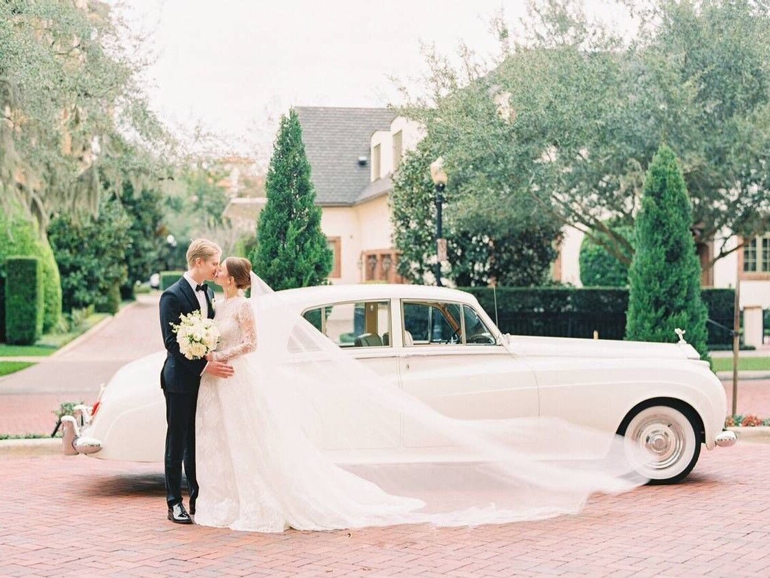 Couple kissing in front of vintage wedding car