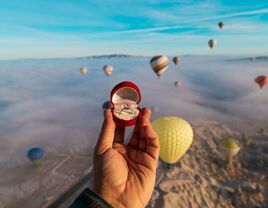 Person holding an engagement ring with the view of hot air balloons in the backdrop