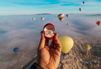 Person holding an engagement ring with the view of hot air balloons in the backdrop