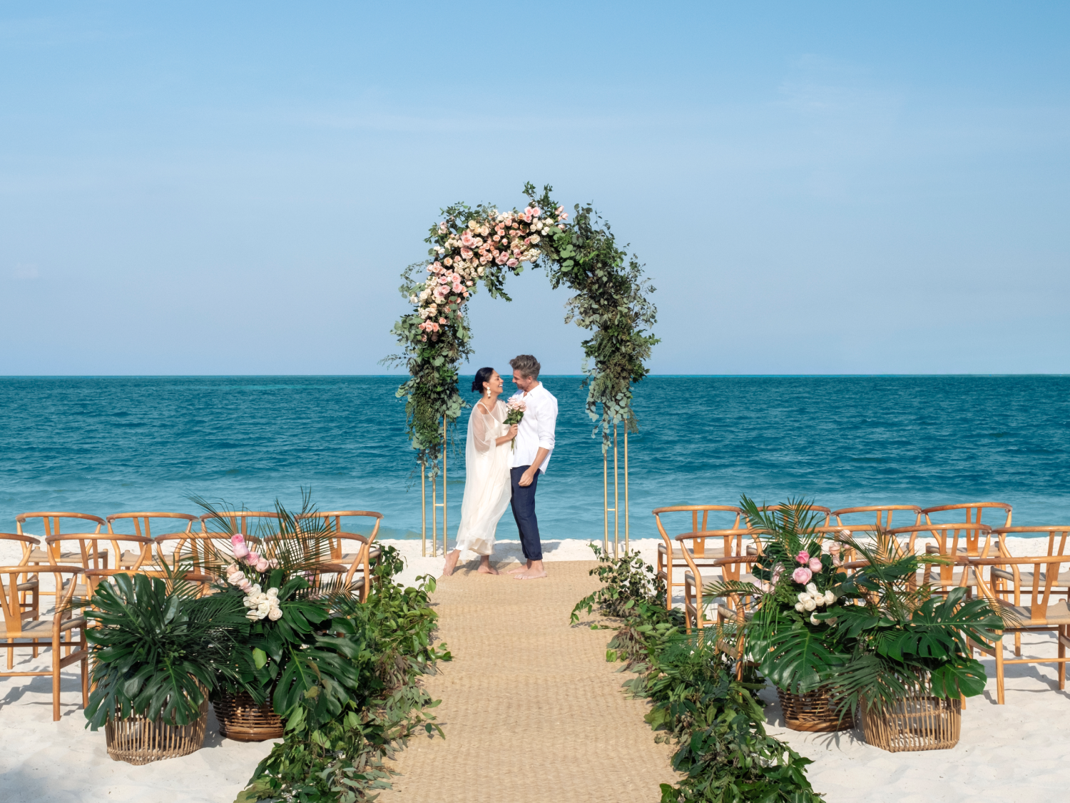 bride and room under flower arch on the beach