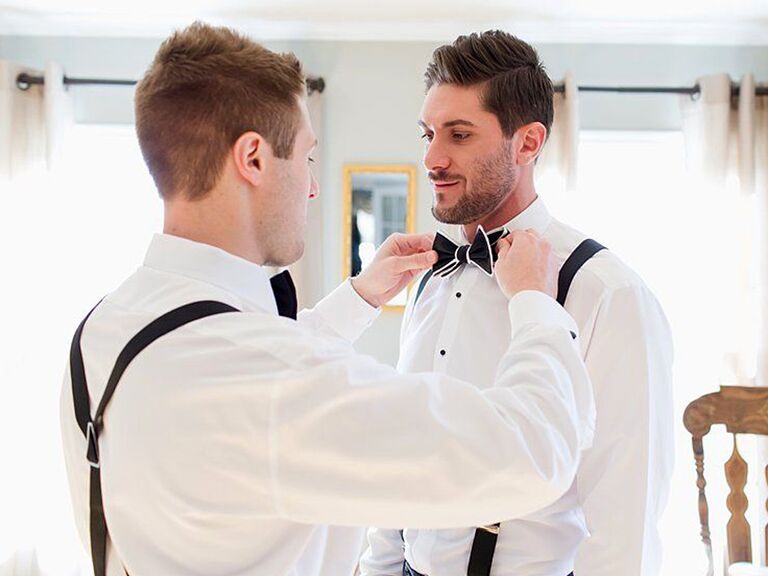 Best man helping groom with bow tie before wedding 