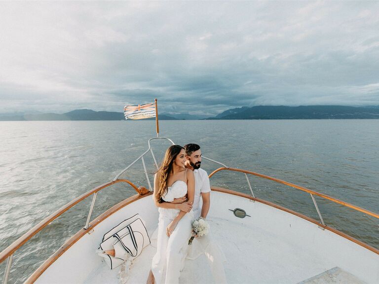Couple stands on the bow of a boat and looks off into the distance. 