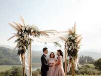 Couple exchanging vows in front of boho floral arch at outdoor summer wedding