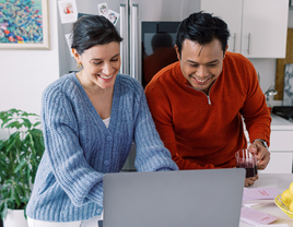 Couple using laptop together and smiling, wedding registry consolidation