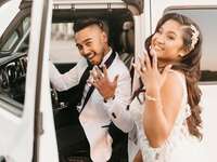 Couple smiles at camera and shows off their new wedding rings standing in front of white jeep