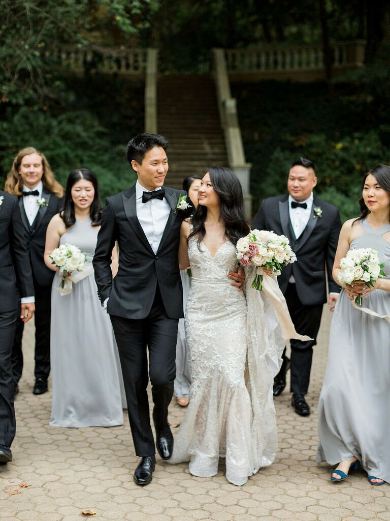 bride and groom wearing formal wedding attire walk with bridesmaids and groomsmen behind them