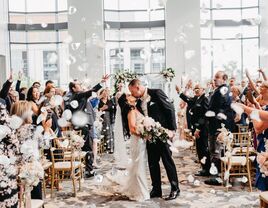 Couple kissing in the middle of the ceremony aisle while guests throw petals