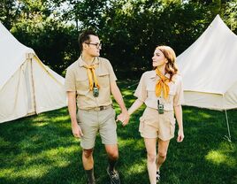 Couple holds hands while wearing summer camp gear. 