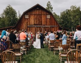 Couple kissing outside the wooden barn venue surrounded by loved ones