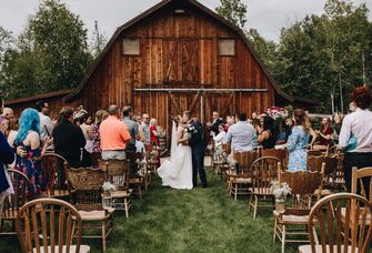 Couple kissing outside the wooden barn venue surrounded by loved ones